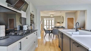 A modern kitchen with a central island, a dining area with chairs, and a large window providing natural light. - Stylish & Spacious 3 Bed Apartment with Parking (Sheffield)