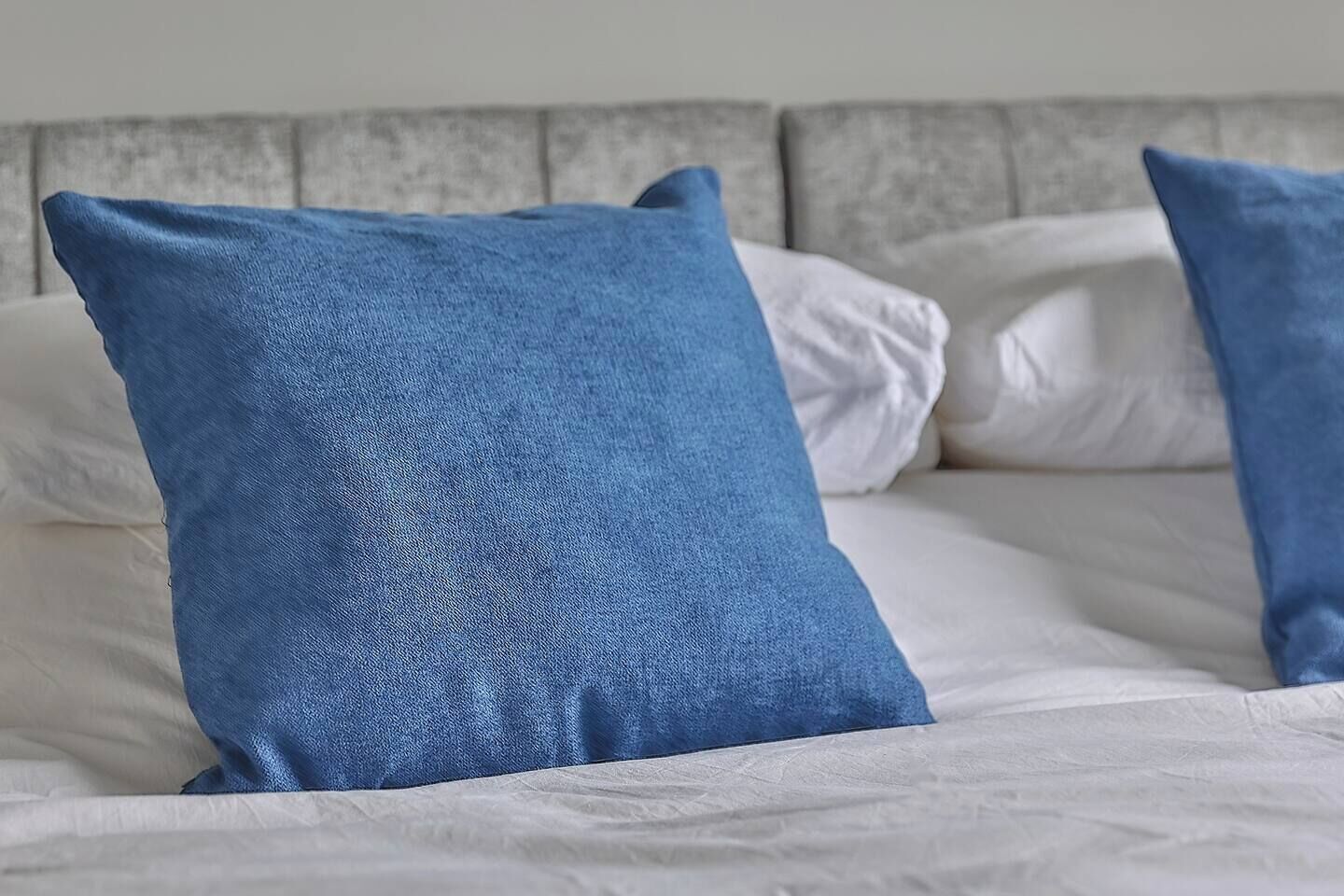 A bed with white bedding and two blue pillows.