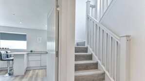 Una cocina moderna con barra, una escalera de madera con barandillas blancas y piso de color claro.