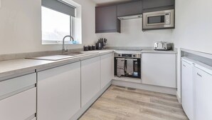 Una cocina moderna con horno empotrado, microondas y tostadora, con armarios blancos y un ventanal grande.