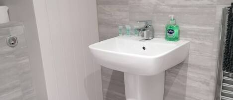 A bathroom with a white pedestal sink, a toilet, and a trash bin.