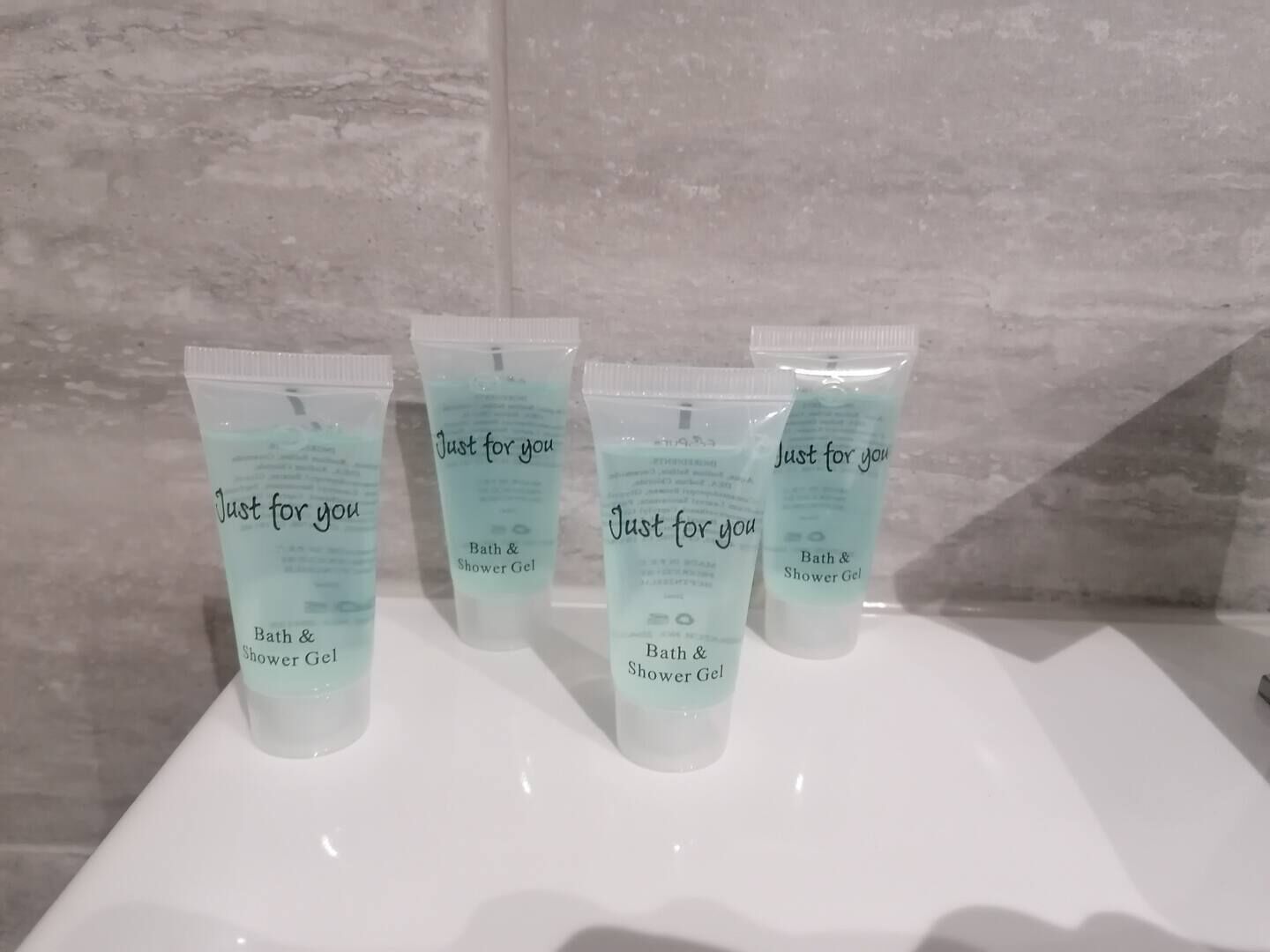 Three bath and shower gel tubes labeled "Just for you" on a white sink against a tiled wall.