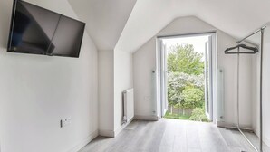 Una habitación moderna con un televisor de pantalla plana montado en la pared, un radiador y un vestidor con barra para colgar ropa.
