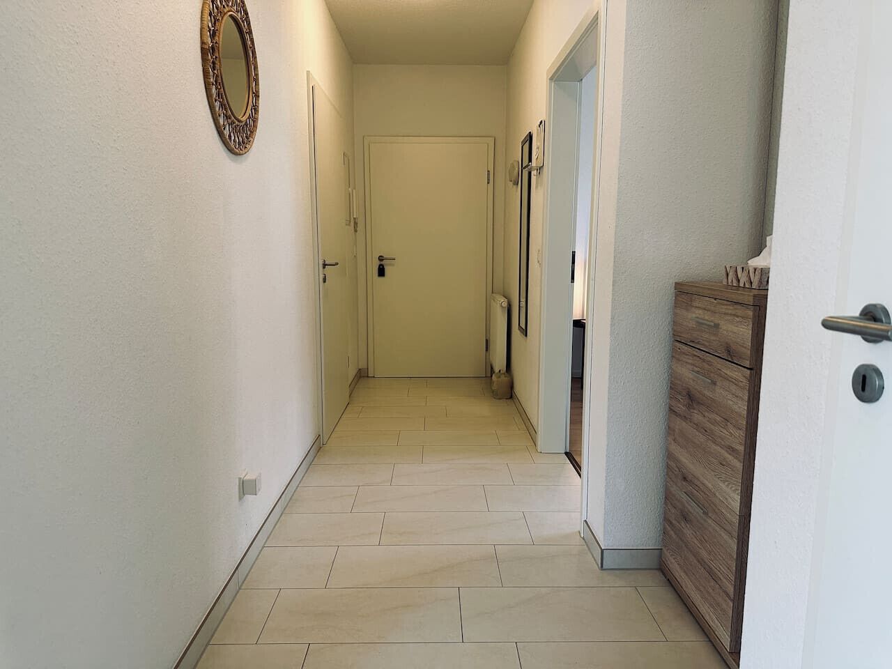 A narrow hallway with a wooden cabinet on the right and a door at the end.