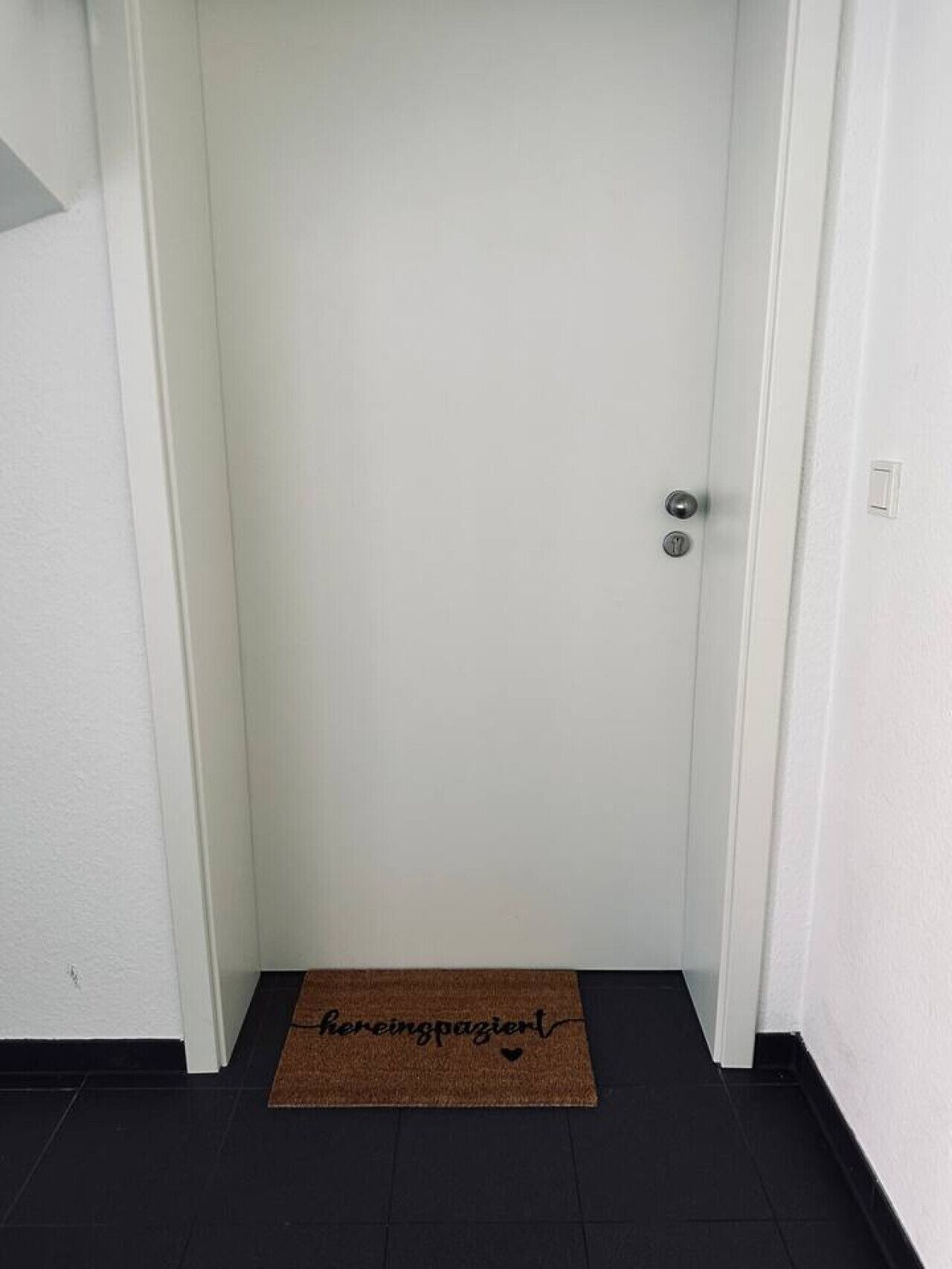 Een witte deur met een deurklink en een kleine lichtschakelaar op de muur.