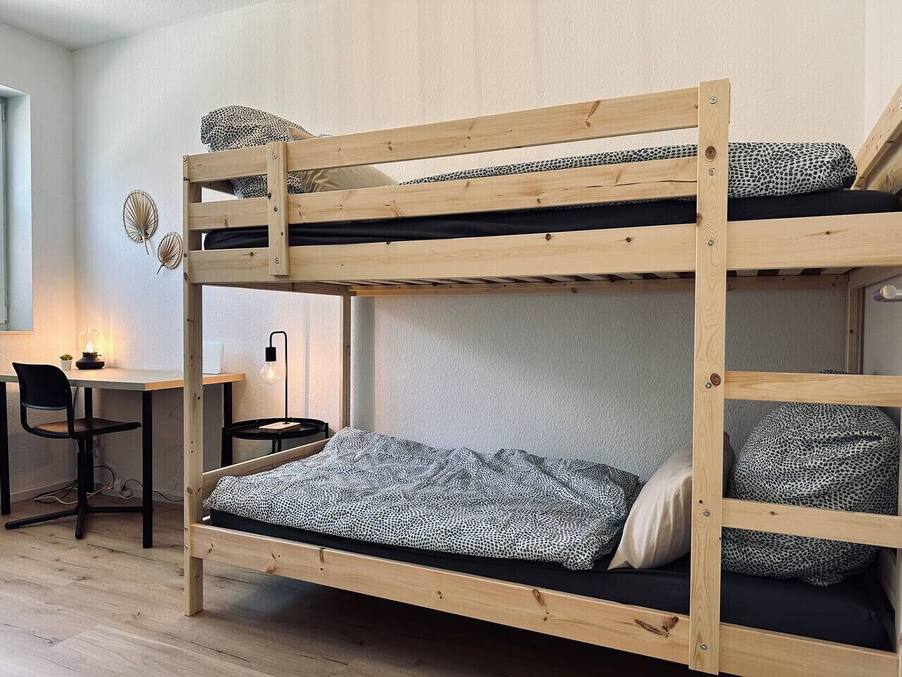Ein Stockbett mit Schreibtisch und Stuhl, einer Lampe sowie dekorativen Wandbildern.