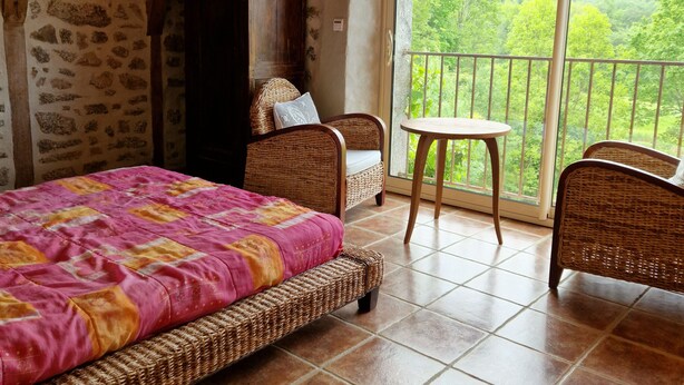 Un dormitorio con cama, una silla, una mesita y un balcón con vistas al bosque.