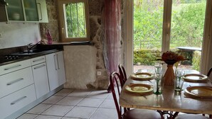 Una cocina rústica con paredes de piedra, suelo de baldosas y una mesa de comedor preparada para cuatro comensales.