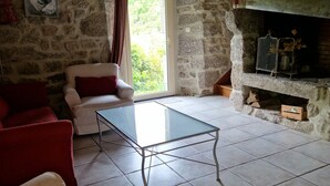 Una habitación rústica con paredes de piedra, una mesa con superficie de vidrio, sofás rojos y beiges, y una chimenea.