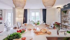 Uma sala de jantar com uma mesa branca posta para refeição, rodeada por cadeiras, e um candelabro acima.