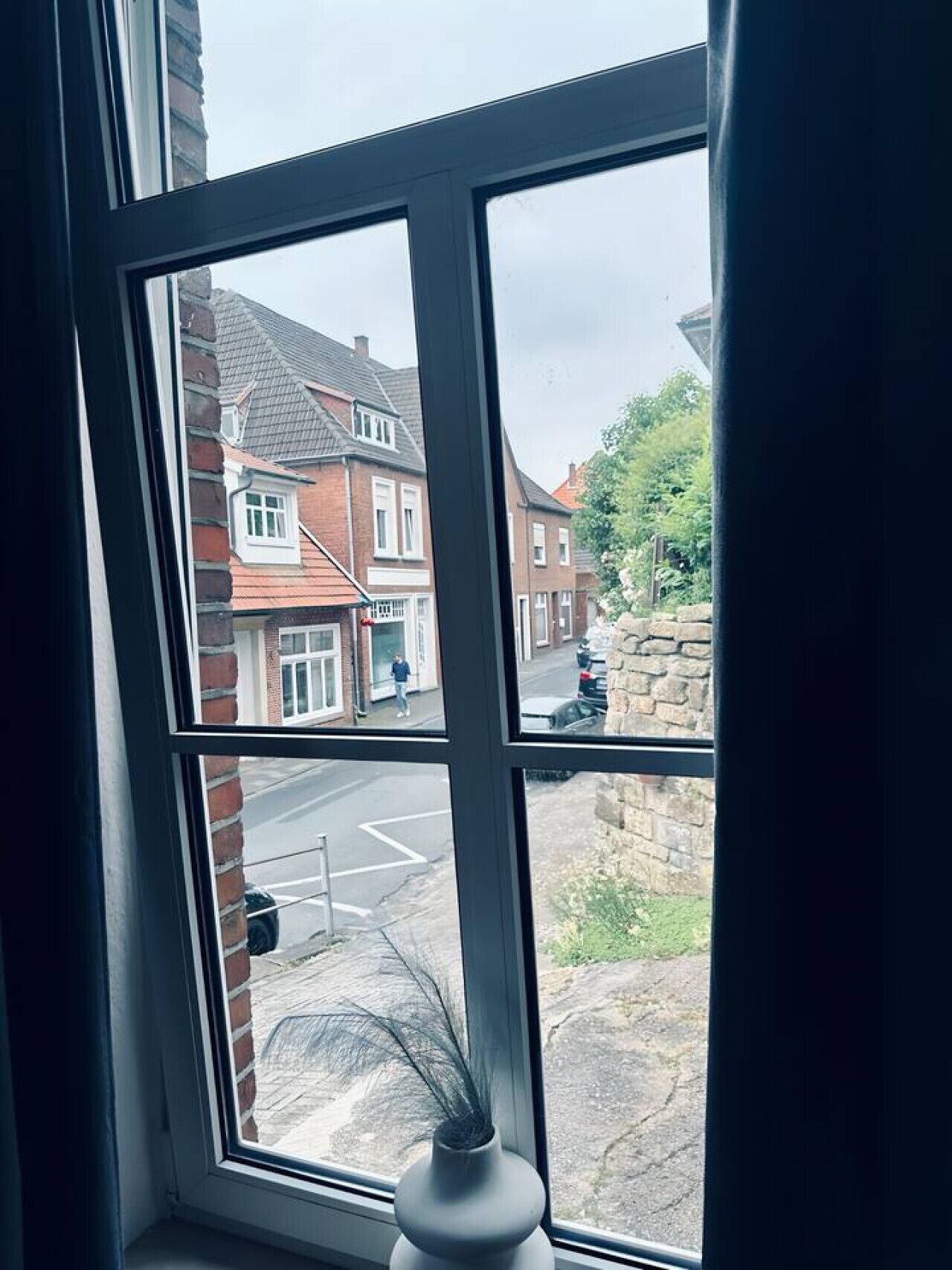Ein Fenster mit Blick auf eine Straße, ein parkendes Auto und eine Steinmauer.