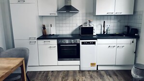 Une cuisine de taille réduite avec des meubles blancs, une cuisinière noire et un lave-vaisselle.