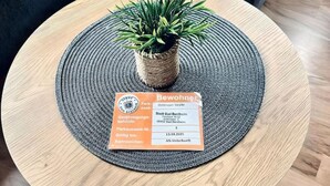 Une table ronde en bois, sur laquelle est posée une nappe en fibres tressées et une petite plante en pot. Un permis de stationnement pour les résidents est affiché sur la nappe.