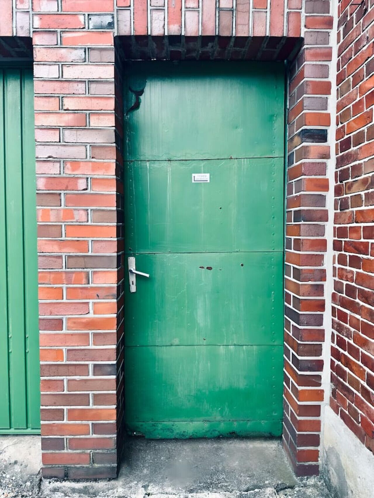 Een groene deur met een bordje, in een bakstenen muur geplaatst.