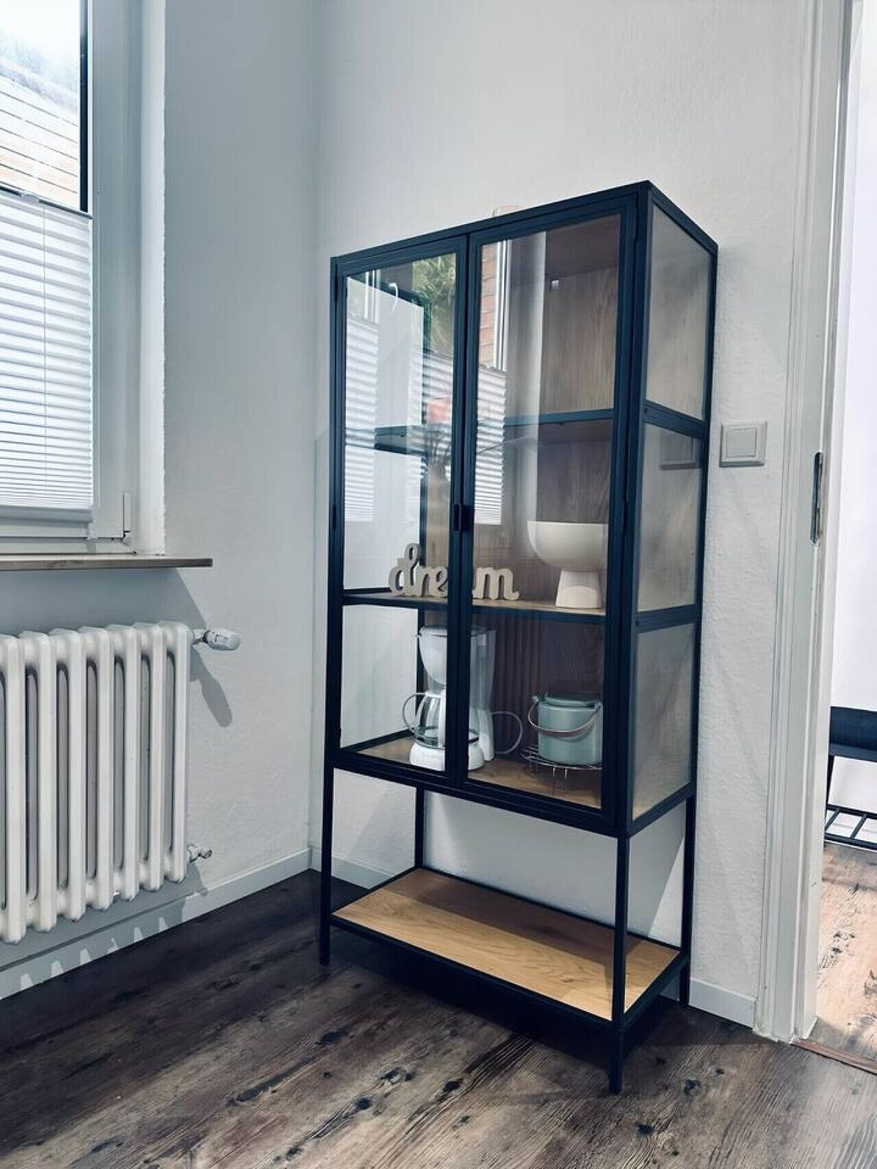 Una stanza angolare con una libreria nera a incasso, un termosifone bianco e un pavimento in legno.