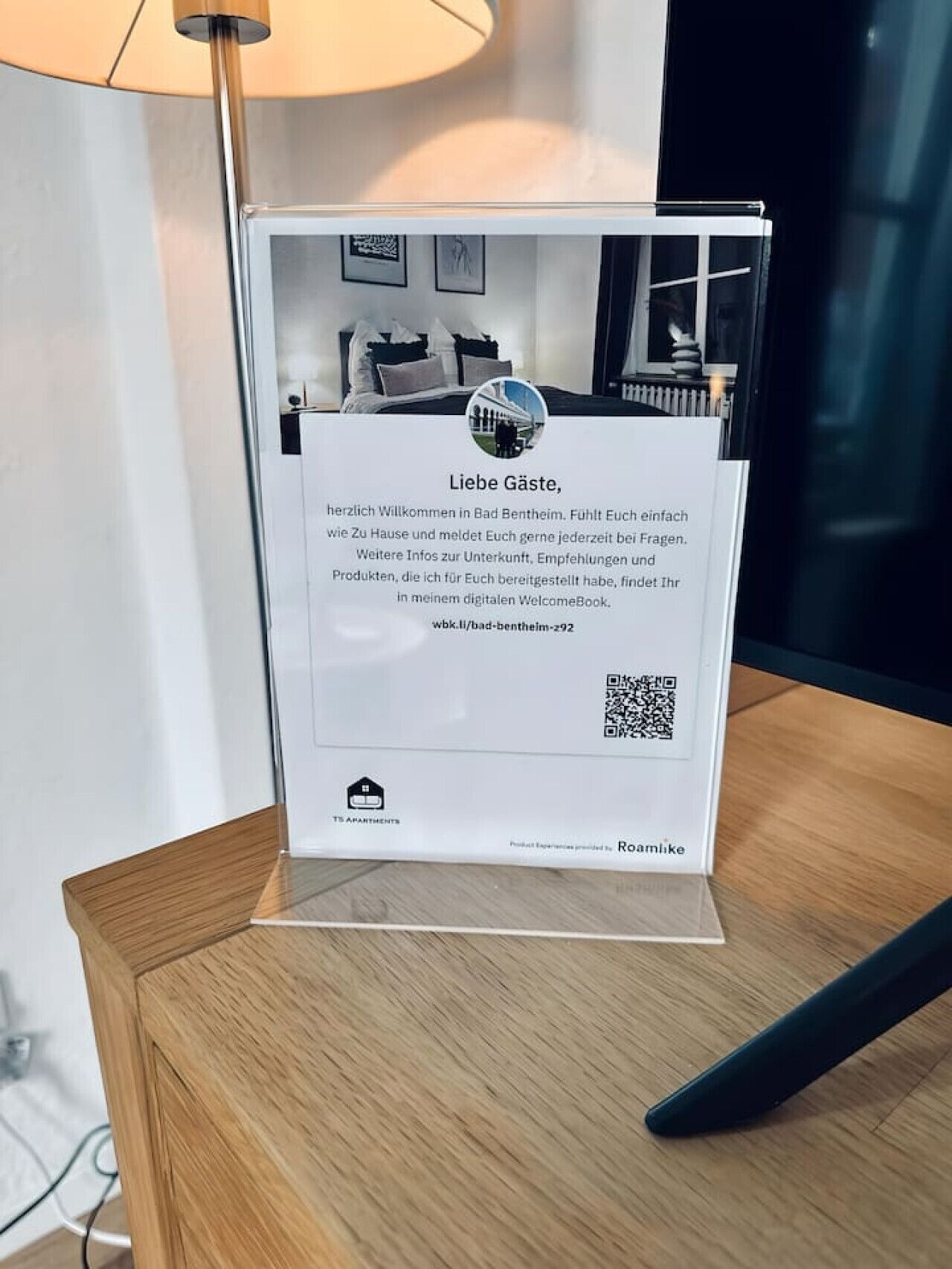 Un panneau d’accueil avec un code QR, un lien vers un guide d’accueil numérique et le logo de TS Apartments.