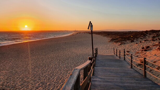A wooden boardwalk leading to a beach with a sunset in the background. - Apartamento do Pinhal by D'Alma Portuguesa (Albufeira)