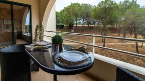 A balcony with a dining table set for two, a small potted plant, and a view of trees and a building in the distance. - Apartamento do Pinhal by D'Alma Portuguesa (Albufeira)