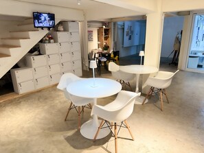 A modern interior with white lockers, a round table with chairs, and a television mounted on the wall. - Letter Better Home (Bangkok)