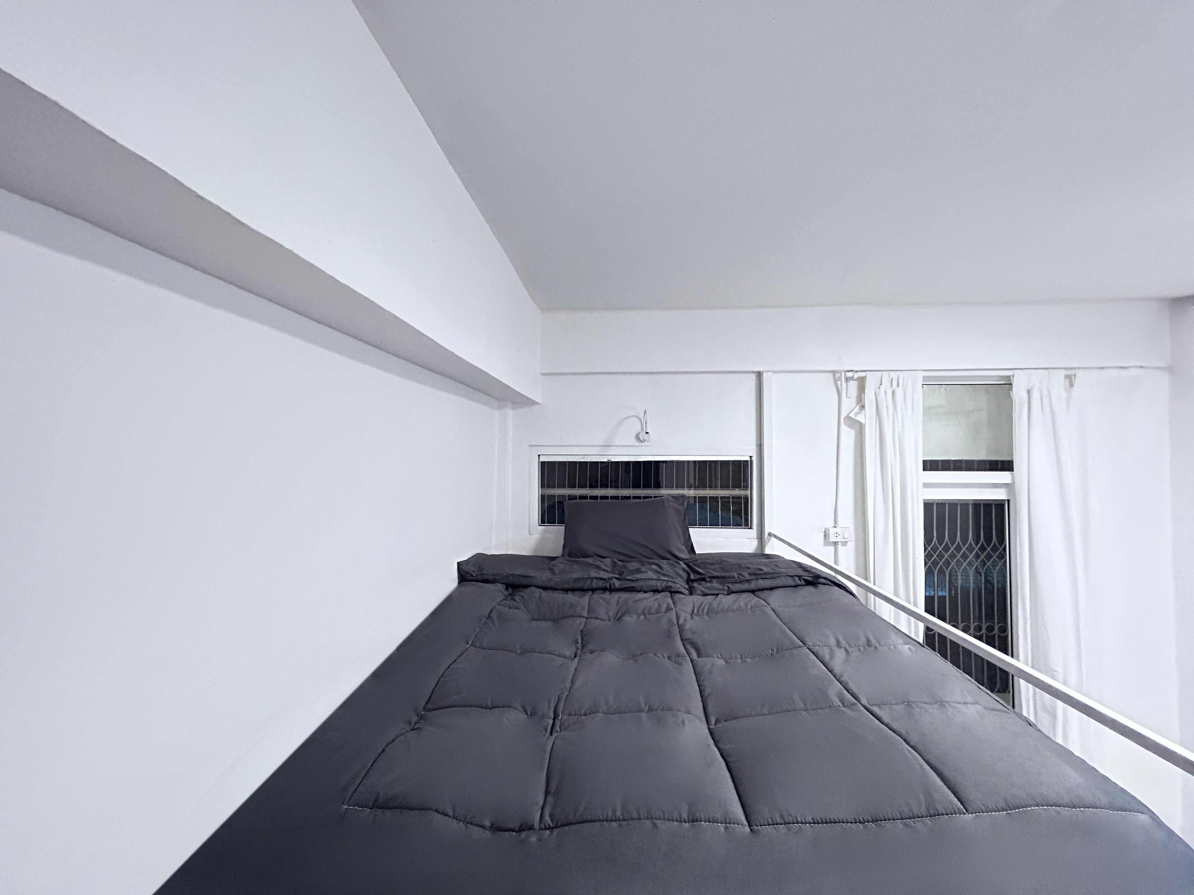 A minimalist room with a bunk bed, white walls, a window with curtains, and a small bedside table.