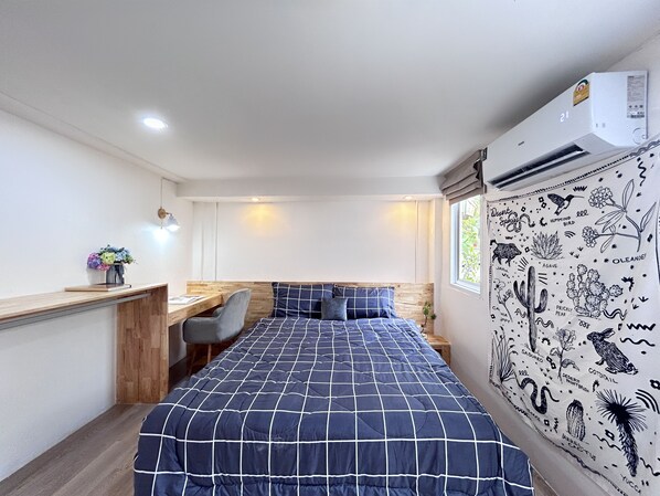 A bedroom with a large bed, a desk, and a chair. There is a window with a view of greenery. - Letter Better Home (Bangkok)