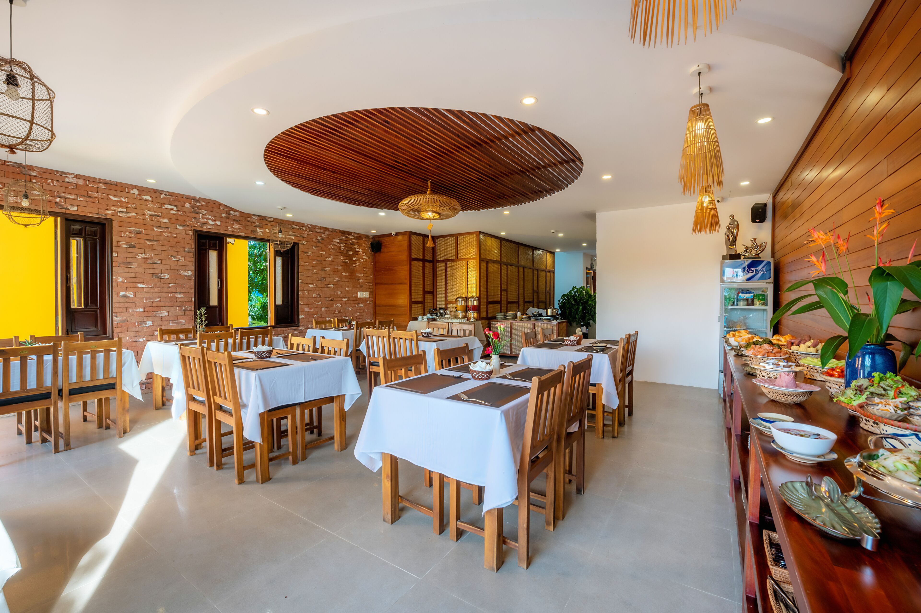 A spacious dining area with multiple tables and chairs, a brick wall, and a wooden ceiling.