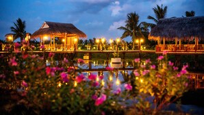 A resort with thatched-roof structures, a water body, and palm trees. - ZEN RETREAT HOI AN (Da Nang)