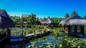 A waterway with overwater bungalows, thatched-roof structures, and a clear blue sky. - ZEN RETREAT HOI AN (Da Nang)