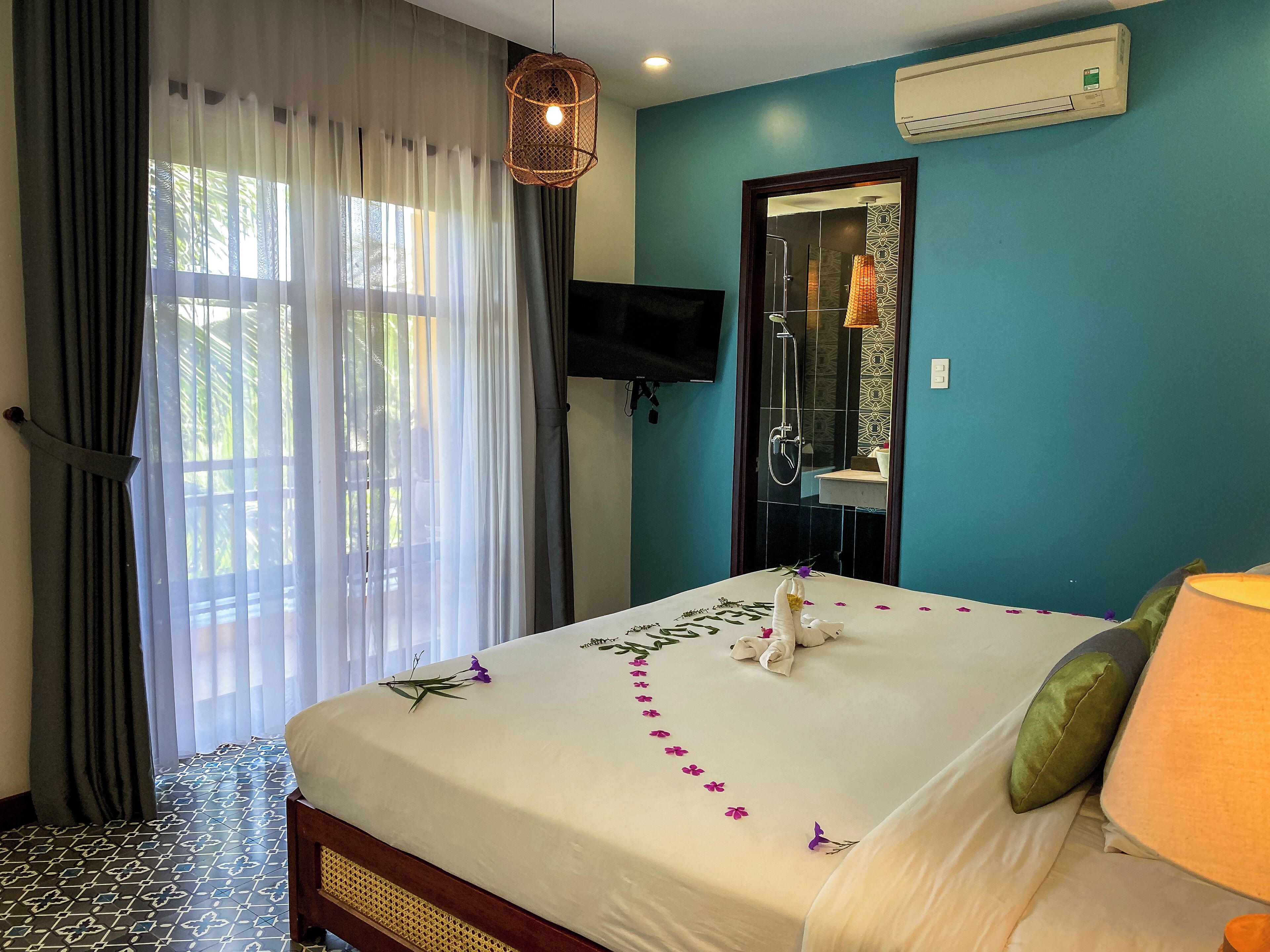 Habitación de hotel con cama, televisor, ducha y ventana con cortinas.