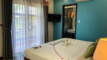 Habitación de hotel con cama, televisor, ducha y ventana con cortinas.