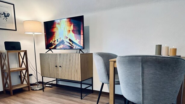 Uma sala de estar moderna com televisão de tela plana, um aparador de madeira, uma poltrona cinza e um abajur.