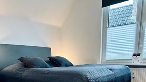 Quarto moderno com cama grande, janela com persianas e radiador.