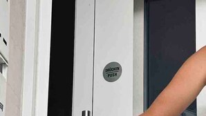 Uma pessoa abrindo uma porta com puxador e botão com a etiqueta "DRÖCKEN PUSH".