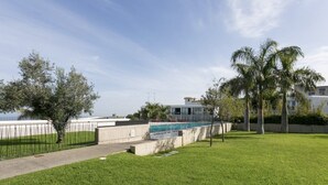 A grassy area with a pathway, palm trees, and a building in the background.