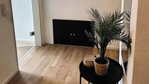 A hallway with a wooden floor, a black console table with a woven basket, a potted plant, and a round mirror with a textured frame. - FeWo Burgblick - Sun terrace & castle view (Bad Bentheim)