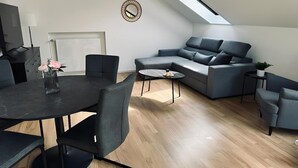 A modern living room with a dark grey sofa, a round coffee table, and a dining table with chairs. - FeWo Burgblick - Sun terrace & castle view (Bad Bentheim)