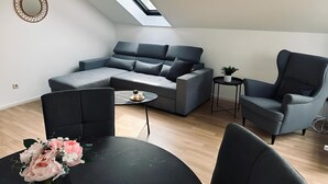 A modern loft apartment with a skylight, grey sofa, armchairs, and a dining table with a vase of flowers. - FeWo Burgblick - Sun terrace & castle view (Bad Bentheim)