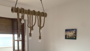 Een slaapkamer met een bed, een hanglamp, een raam met jaloezieën en een schilderij aan de muur.