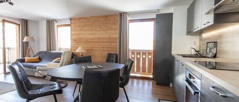 A modern living room with a round table and chairs, a sofa, and a kitchen area with cabinets and a stove.