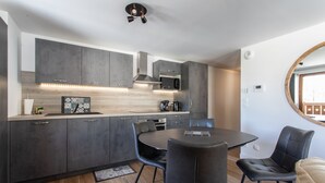 A modern kitchen with grey cabinets, a central island, and a dining area with black chairs. - Le Bierge - Station de ski accessible à pied (Vars)