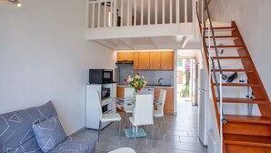A compact living space with a dining area, kitchenette, and a wooden staircase.