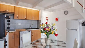 A modern kitchen with wooden cabinets, a dishwasher, and a refrigerator. There is a vase with flowers on the table.