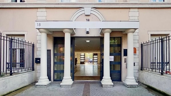 Une entrée d’immeuble avec des colonnes, une enseigne portant le numéro « 18 » et une porte en verre.