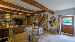A rustic dining area with a stone wall, wooden beams, a fireplace, and a staircase.