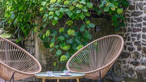 Two wicker chairs with a small round table and two cups, set against a stone wall and lush greenery.