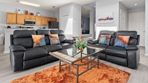 Een moderne woonkamer met twee zwarte leren banken, een glazen salontafel en een feloranje vloerkleed.