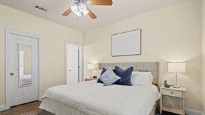 A bedroom with a large bed, two bedside tables with lamps, a ceiling fan, and a door with a mirror. - Welcome!  This apartment offers a spacious and comfortable place to stay.   (Hammond)