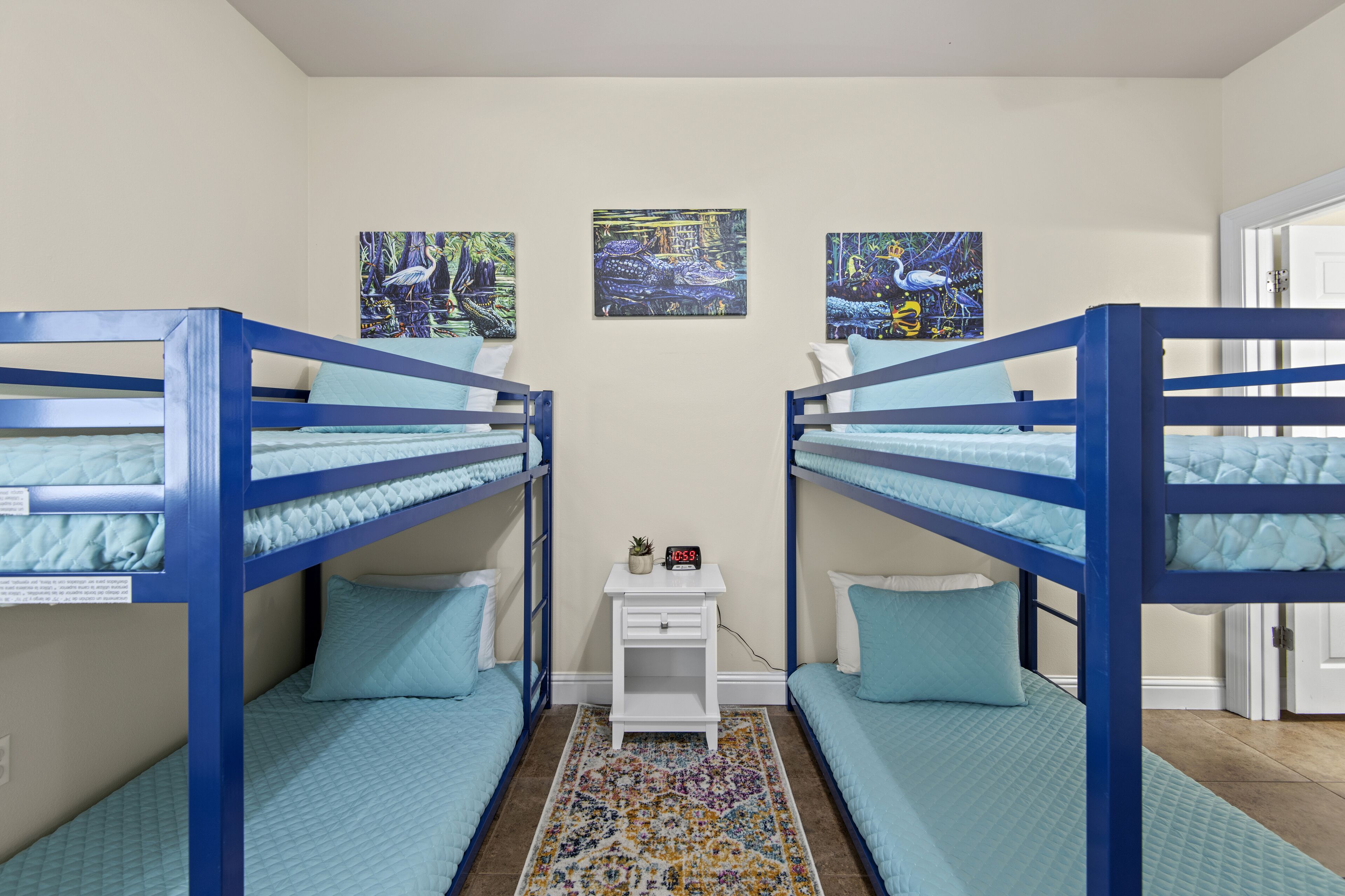 A room with bunk beds, a small white nightstand with a clock, and two framed artworks on the wall.