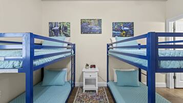 A room with bunk beds, a small white nightstand with a clock, and two framed artworks on the wall.