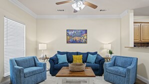 A living room with a blue sofa, two matching armchairs, a wooden coffee table, and a ceiling fan. - Welcome!  This apartment offers a spacious and comfortable place to stay.   (Hammond)